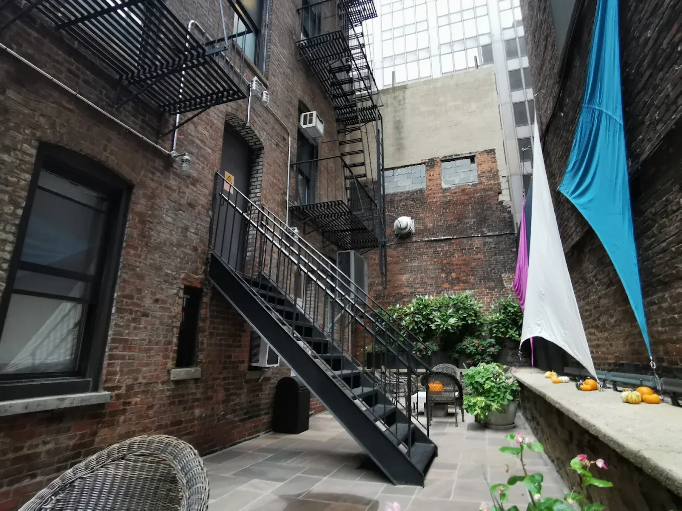 The rear courtyard at Seton Residence, with planted beds, shade sails and the building's fire escape overhead
